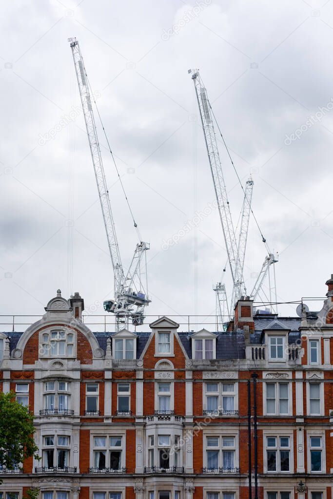 Two white cranes emerge against a cloudy sky and behind a row of typical brick houses in London, UK.