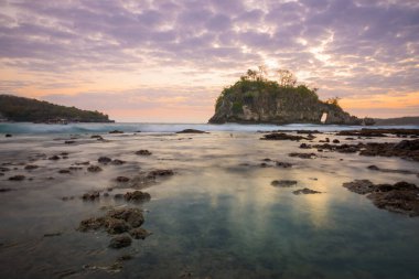 Kristal Koyu 'nda gelgitle birlikte gün batımı kaya adası boyunca ilerliyor. Deniz suyu Nusa Penida, Bali, Endonezya' daki kaya ve su birikintilerinin üzerine dökülüyor.