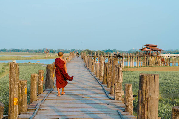 Mandalay, Myanmar - 3 Jun 2014:  A Buddhist monk walks on the U-Bein teakwood bridge at sunrise, in Mandalay, Myanmar