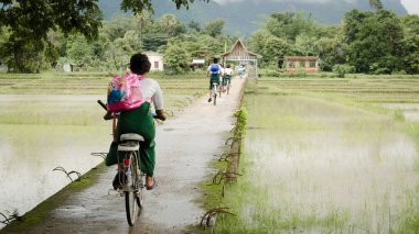 Hpa An, Myanmar - 13 Jun 2014: Children in school uniform ride a bicycle on a concrete bridge across the paddy fields, around Hpa An town in southern Myanmar. clipart