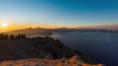 Güneşin volkanik bir tepenin üzerinde batışı ve bir krater gölü üzerinde yansıması, Oregon, ABD 'deki bir ulusal parktaki bir tepe uçurum manzarası.