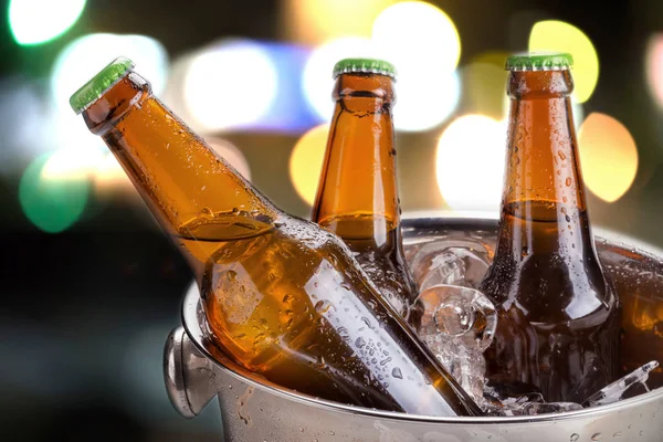 cold bottles of beer in bucket with ice on bokeh background
