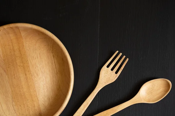 Spoons, forks and Dish made of wood on the black wooden background.