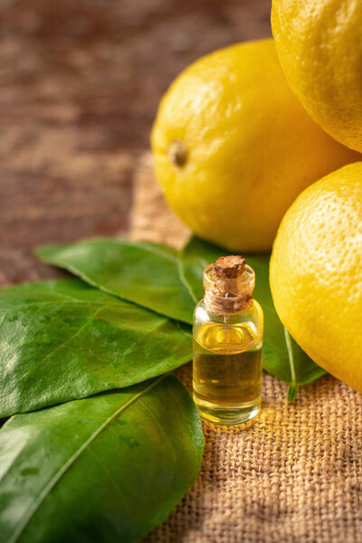 Bottle with Essential Oil of Lemon peel and leaves on wooden table