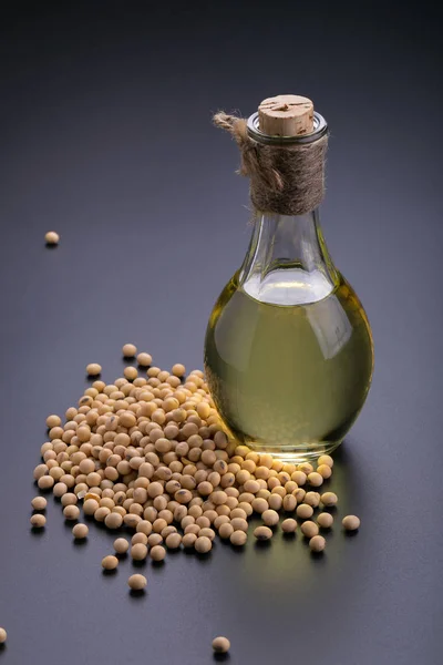 Soybeans in a wooden bowl and soybean oil on a black background.