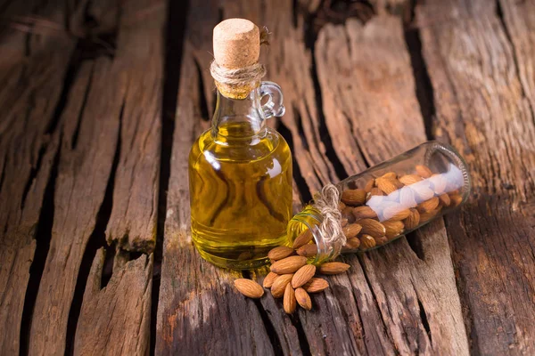 Bottle of almond oil and almonds on old wooden table background