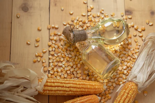 Кукурузное масло и кукурузные зерна на фоне натурального дерева — стоковое фото