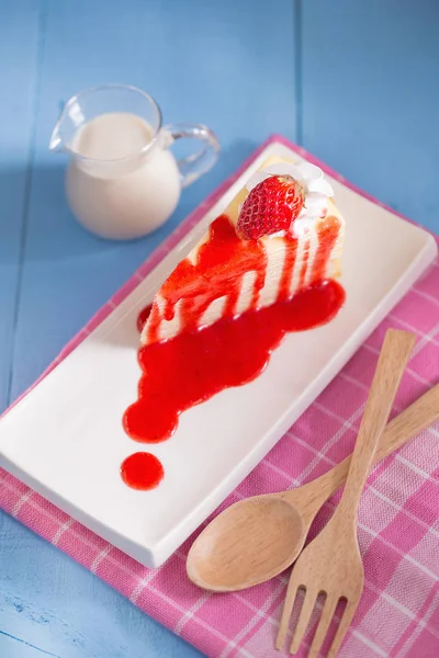 Strawberry crepes cake with strawberry sauce and latte on blue table with wooden fork and spoon.