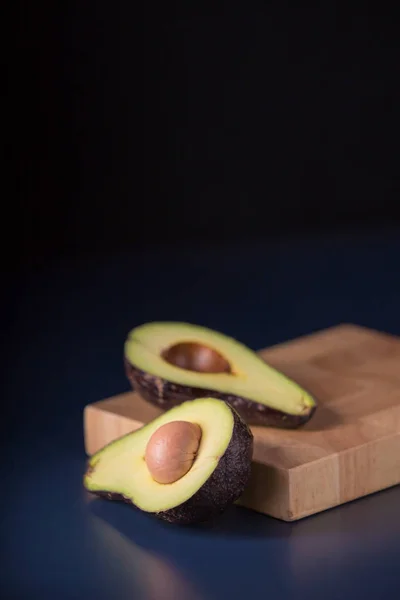 Abacate cortado pela metade numa mesa rústica. Abacate fresco em backgro preto — Fotografia de Stock