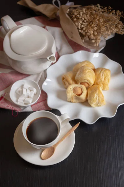 Tasty mini sausages in bread rolls and Cup of hot coffee on dark background