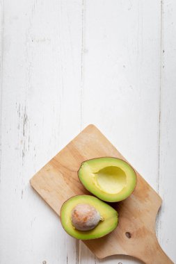 Beyaz ahşap masa üzerinde ikiye taze organik avokado dilimlenmiş