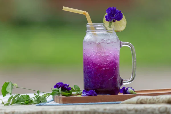 鲜紫色蝴蝶豌豆或蓝色豌豆花和柠檬汁在玻璃与绿色模糊背景 — 图库照片