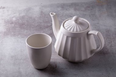 Çaydanlık kreması, fincan ve çay tabağı çimento tahtasında.