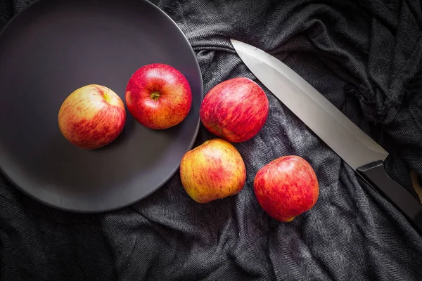 Red apples in a black bowl on a Black fabric background.