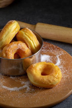 Koyu bir masa arkasındaki tahta tabakta şekerli çörekler.