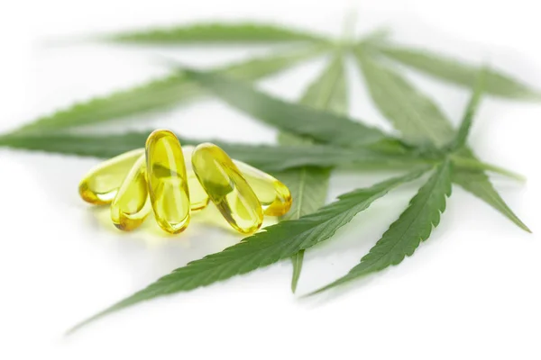 Esrar temel yağ kapsülleri beyaz arka planda esrar yaprakları ile.