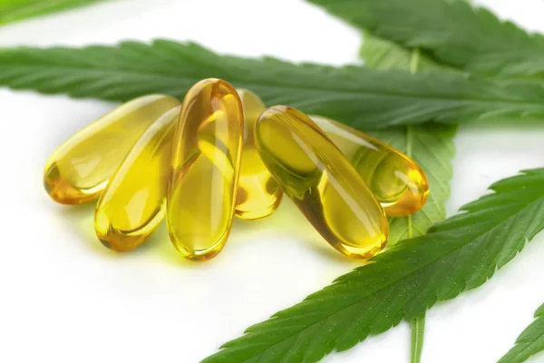 Esrar temel yağ kapsülleri beyaz arka planda esrar yaprakları ile.