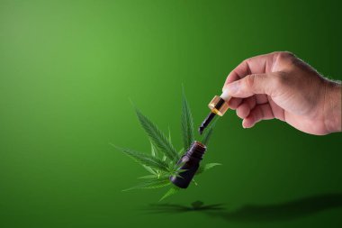 Hand holding pipette of Cannabis oil over a bottle of Formula CB clipart
