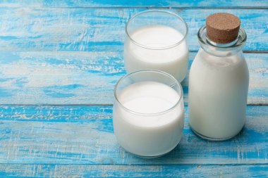 Mavi ahşap bir masada bir şişe süt ve bir bardak süt, healt