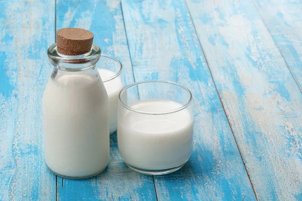 Láhev mléka a sklenice mléka na modrém dřevěném stole, léčený — Stock fotografie