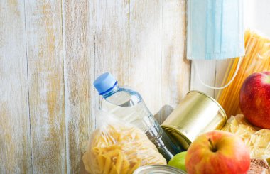 Çeşitli yiyeceklerle birlikte bağış kutusu. Koruyucu tıbbi maske, yağ, konserve ürünler, mısır gevreği ve meyve içeren açık bir karton kutu..