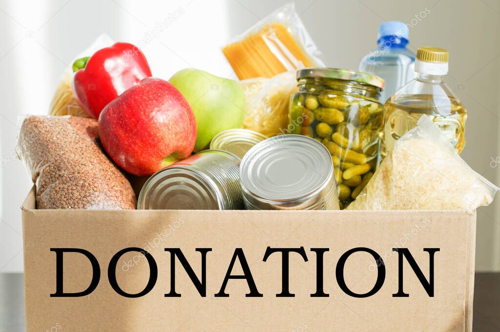 Donation box with various food. Open cardboard box with butter, canned goods, cereals and fruits.