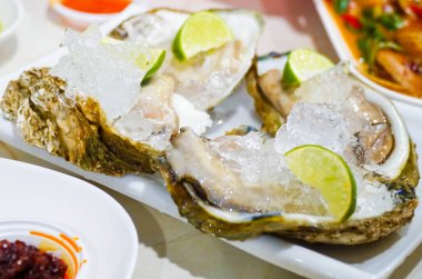 Taze istiridye, istiridye, limon ve buzla servis edilen bir tabağa yakın plan. Sağlıklı deniz ürünleri. Restoranda şampanyalı istiridye yemeği. Gurme yemekleri.