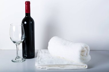 Kırmızı şarap, şarap bardakları ve beyaz arka planda beyaz havlular ve aşık kalpler. Otelin yatak odasındaki beyaz arka plana güzel beyaz havlular yerleştiriliyor..