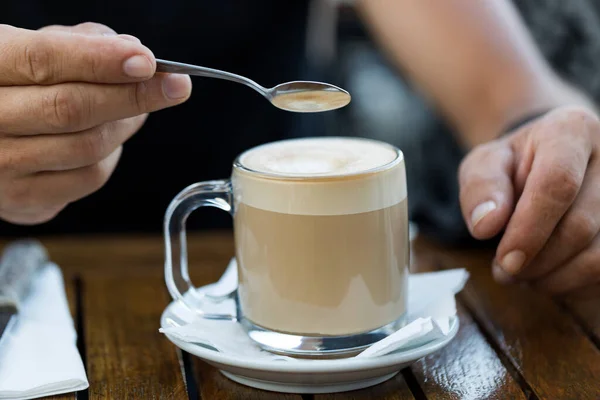 The men holding coffee spoon and stirring hot coffee on wooden table in the morning