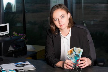 Bir tomar para tutan ve gösteren bir iş kadını, İsrail para banknotları şekekliyor. Finansal tema.