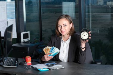 Zaman para konseptidir. Güzel bir iş kadını elinde çalar saat ve ILS şekelleri tutuyor. Zaman yatırım konsepti. Bayan patron. Başarı kariyer serveti. Reklam için boşluk kopyala.