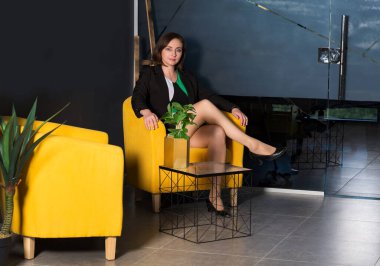 Sarı ofis koltuğunda oturan mutlu esmer kadın. Gri arka planda yalnız başına rahatlıyor.