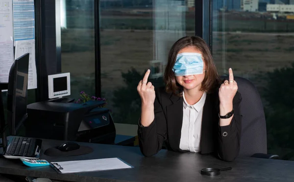 Wrong way to wear a mask against coronavirus - Beautiful Brunette Woman wearing mask to cover her eyes showing grimace face and showing double rude gesture, dark background. Being funny and crazy