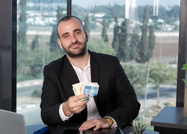 Takım elbiseli kendine güvenen bir işadamı bir sürü para tutuyor ILS şekelleri. Zaman yatırımı, maaş, kredi ve rüşvet konsepti. Başarı kariyer serveti. Reklam için boşluk kopyala.