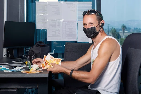 Man holds Israel shekels banknotes. Financial theme. Horizontal view. Money matters. Male sitting at his desk in protective mask, counting money