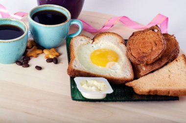 Tahta kesme tahtasındaki kahvaltı beyaz arka planda, kırpma yolu ile izole edilmiş. Seramik kasede kızarmış yumurta, iki fincan espresso ve tereyağı.