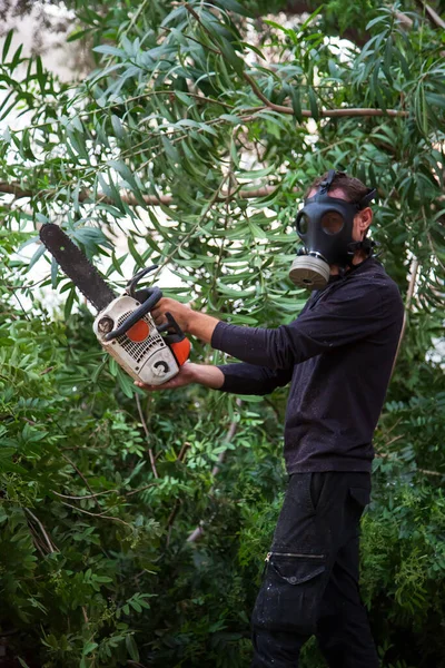 Man with the chainsaw in a gas mask. Dangerous job. Powerful chainsaw. Lumberjack hold chainsaw. Gardener lumberjack equipment. Working in the garden near home during quarantine.