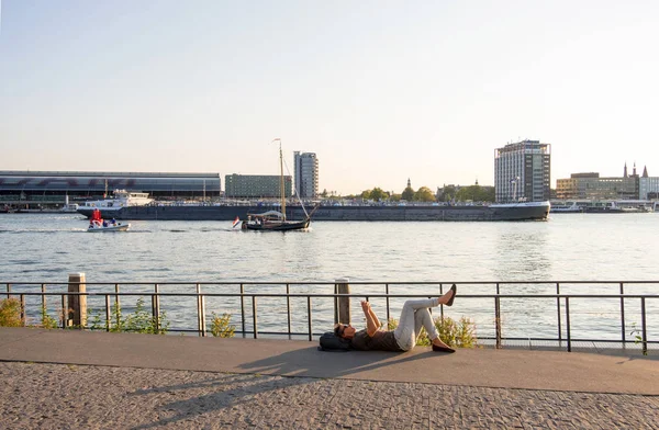 Mujer descansando en la orilla del río Amstel sobre el telón de fondo del puerto y la estación central de Ámsterdam — Foto de Stock