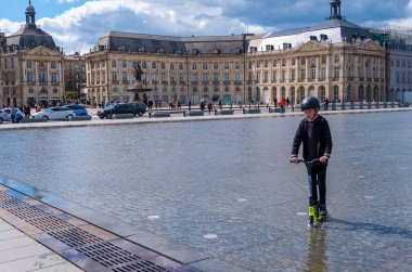 Bir çocuk Bordeaux 'da Place de la Bourse önünde Miroir d 'eau üzerinde bir Scooter sürmek, Fransa