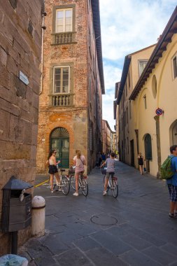 Lucca, İtalya - 14 Ağustos 2019: Eski dar ortaçağ caddesinde bisikletli kızlar, tarihi Lucca, Toskana 'nın merkezinde kafe ve dükkanlar