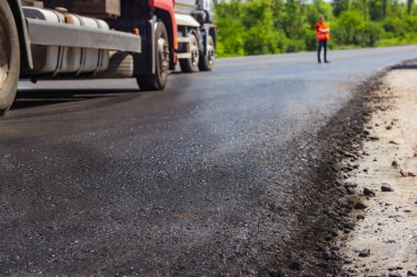 Yakın zamanda arka fondaki üniformalı inşaatçılarla döşenmiş olan yeni bir yol ve kaldırım makinesinin arka planını kapat.