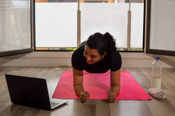 Kafkasyalı kız elinde dizüstü bilgisayarla oturma odasında yoga yapıyor.