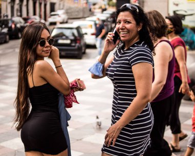 Güneşli bir yaz gününde cep telefonlarını kullanarak şehirde yürüyen genç kadınların seçici odak noktası