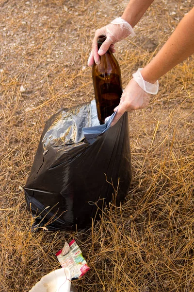 Bir çayırda plastik çöp toplayan beyaz bir kadının elleri.