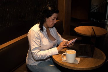 Kafeteryadaki beyaz kadın telefonda konuşurken dizüstü bilgisayarla çalışıyor ve kahve içiyordu.