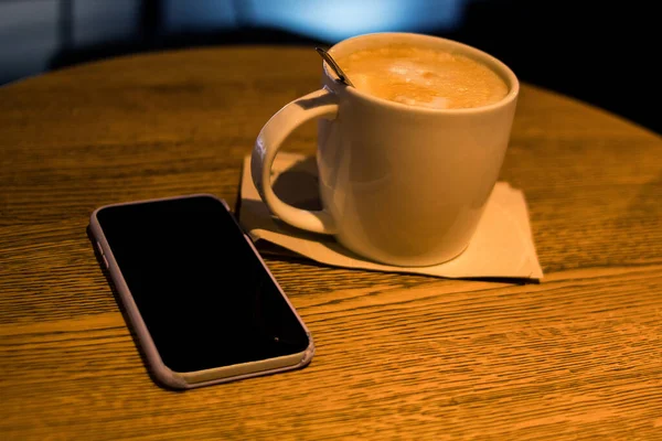 Kahve dükkanındaki bir masada yanında telefon olan beyaz bir fincan kahve.