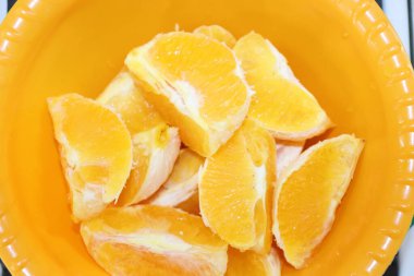 Sarı bir kasede soyulmuş portakallar.