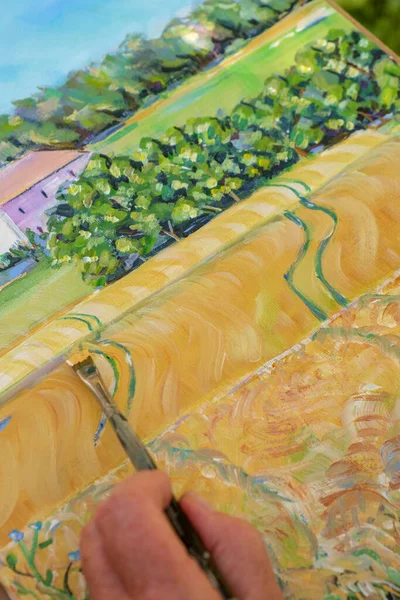 Close up of the hand and brush of a lady artist painting a landscape.