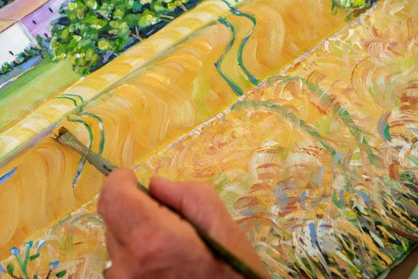 Close up of the hand and brush of a lady artist painting a landscape.