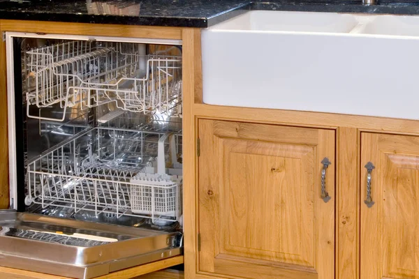 Empty open dishwasher next sink and kitchen cupboards